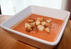 a white bowl filled with soup on top of a wooden table next to a window