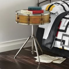 a table with books on top of it next to a bed in a room that has hardwood floors and white walls