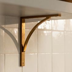 a wooden shelf mounted to the side of a white tiled wall with a wood handle