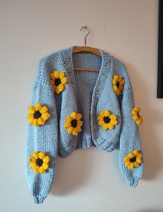 a blue sweater with sunflowers on it hanging from a hook in a room