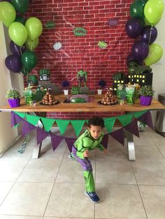 a little boy standing in front of a table with green and purple decorations on it