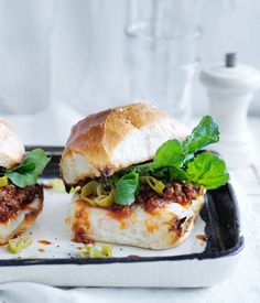 two sandwiches with meat, cheese and vegetables on a black plastic tray sitting on a white tablecloth