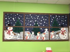 the snowmen are in front of the window on the green wall, and there is a christmas tree behind them