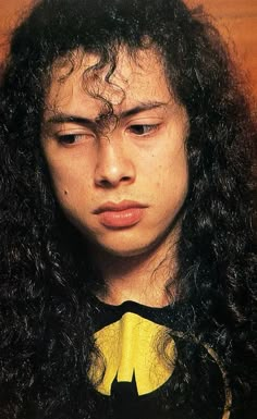 a young man with long curly hair wearing a batman shirt