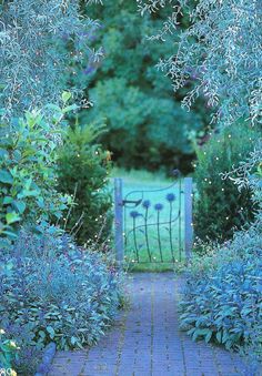 an open gate in the middle of a garden filled with blue flowers and greenery