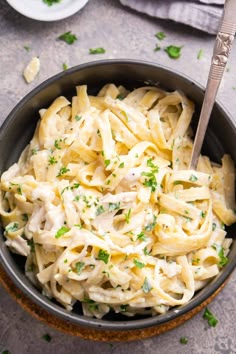 a bowl filled with pasta and parsley on top of a table next to a fork