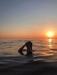 a person in the water at sunset with their back to the camera, and one hand on his head