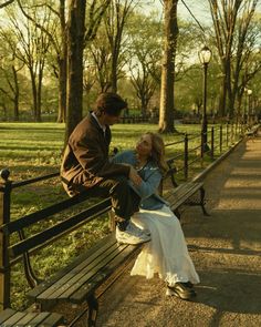 a man and woman sitting on a bench in the middle of a city park, looking at each other