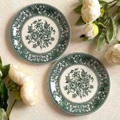 two green and white plates sitting on top of a table next to some flower arrangements