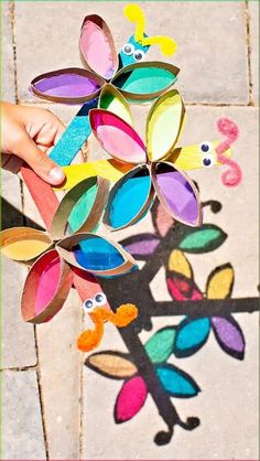 a child's hand holding a paper flower made out of colored construction paper on a tile floor