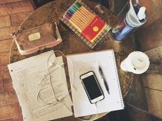 a table topped with books, papers and a cell phone on top of a wooden table