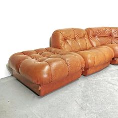 a brown leather couch sitting on top of a cement floor next to a white wall