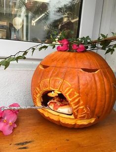 a carved pumpkin sitting on top of a wooden table next to a pink flower pot