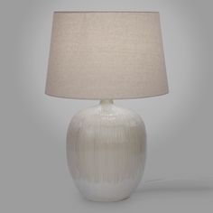 a white table lamp with a beige shade on the base and a light grey background