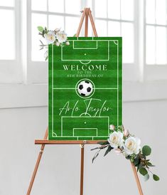 an easel with a welcome sign on it and flowers in the corner next to it