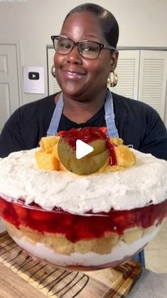 a woman holding a large cake with fruit toppings on it's top and smiling at the camera