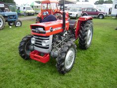 an orange tractor parked on top of a lush green field next to other cars and trucks