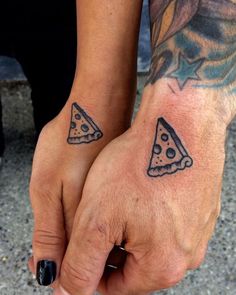 two people are holding hands with tattoos on their arms and one has a slice of pizza