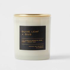 a white candle with gold lid and label on the top that says olive leaf + oud