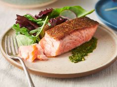 a piece of salmon on a plate next to a fork and some greens with pesto