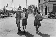 three women walking down the street carrying babys in their arms and two men with hats on