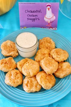 a blue plate topped with chicken nuggies next to a small bowl of dip