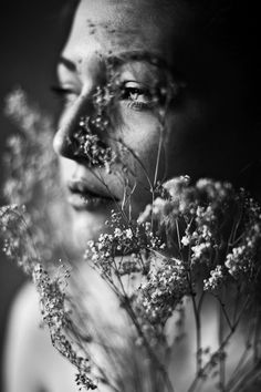 black and white photograph of a woman with flowers in front of her face, looking up at the sky