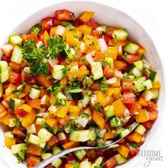 a white bowl filled with cucumber, tomato and cilantro salad next to a spoon