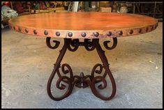 a wooden table with metal legs and an ornate design on the top, sitting in a garage