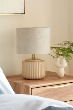 a white vase sitting on top of a wooden table next to a lamp with a green plant in it