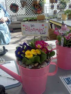 two pink mugs filled with flowers sitting on top of a table next to a sign