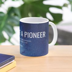 a blue coffee mug sitting on top of a wooden table next to a book and plant