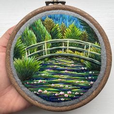 a hand embroidered picture of a bridge over a pond with water lilies in it