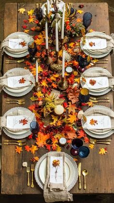 a wooden table topped with lots of white plates and place settings covered in fall leaves