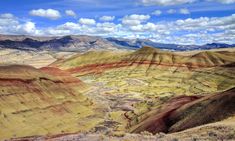 the mountains are painted in different colors and sizes, with clouds above them on a sunny day