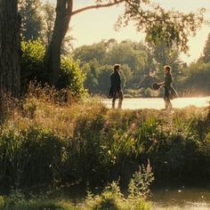 two people standing on the edge of a body of water with trees in the background