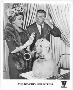 an old black and white photo of two people petting a poodle in front of a window