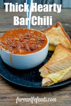 a black plate topped with a bowl of chili and two pieces of toast