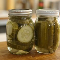 two jars filled with pickles sitting on top of a wooden table