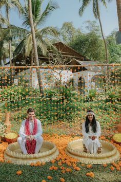 two people sitting on small beds in the middle of some orange flowers and palm trees