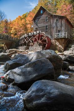 an old mill sits on the edge of a river with rocks in front of it