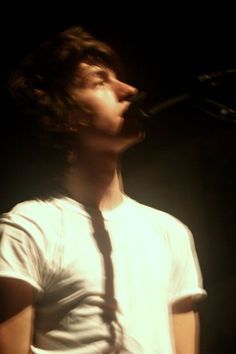 a young man wearing a white shirt and tie singing into a microphone in the dark