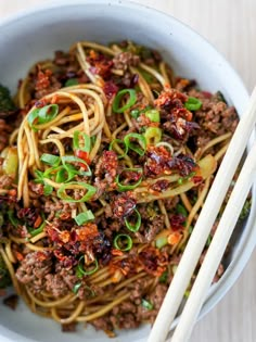 a white bowl filled with noodles, meat and broccoli next to chopsticks