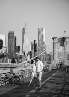 black and white photograph of two people walking across a bridge in front of the city skyline