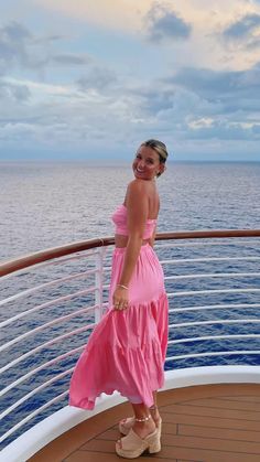 a woman in a pink dress standing on the deck of a cruise ship looking at the camera