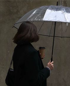 a woman walking down the street while holding an umbrella over her head with a cup of coffee