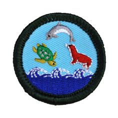 an embroidered patch with a dolphin and turtle in the ocean on blue water, surrounded by waves