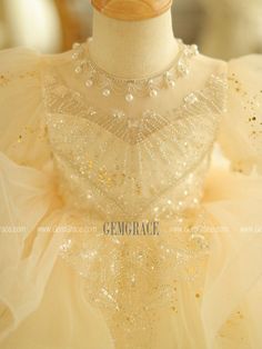 a white dress with gold sequins and pearls on the neckline is displayed in front of a mannequin