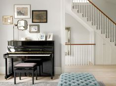 there is a piano in the living room with pictures on the wall and stairs to the second floor