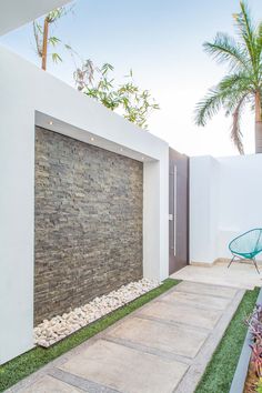 an outdoor area with grass, rocks and a blue chair in front of a white wall